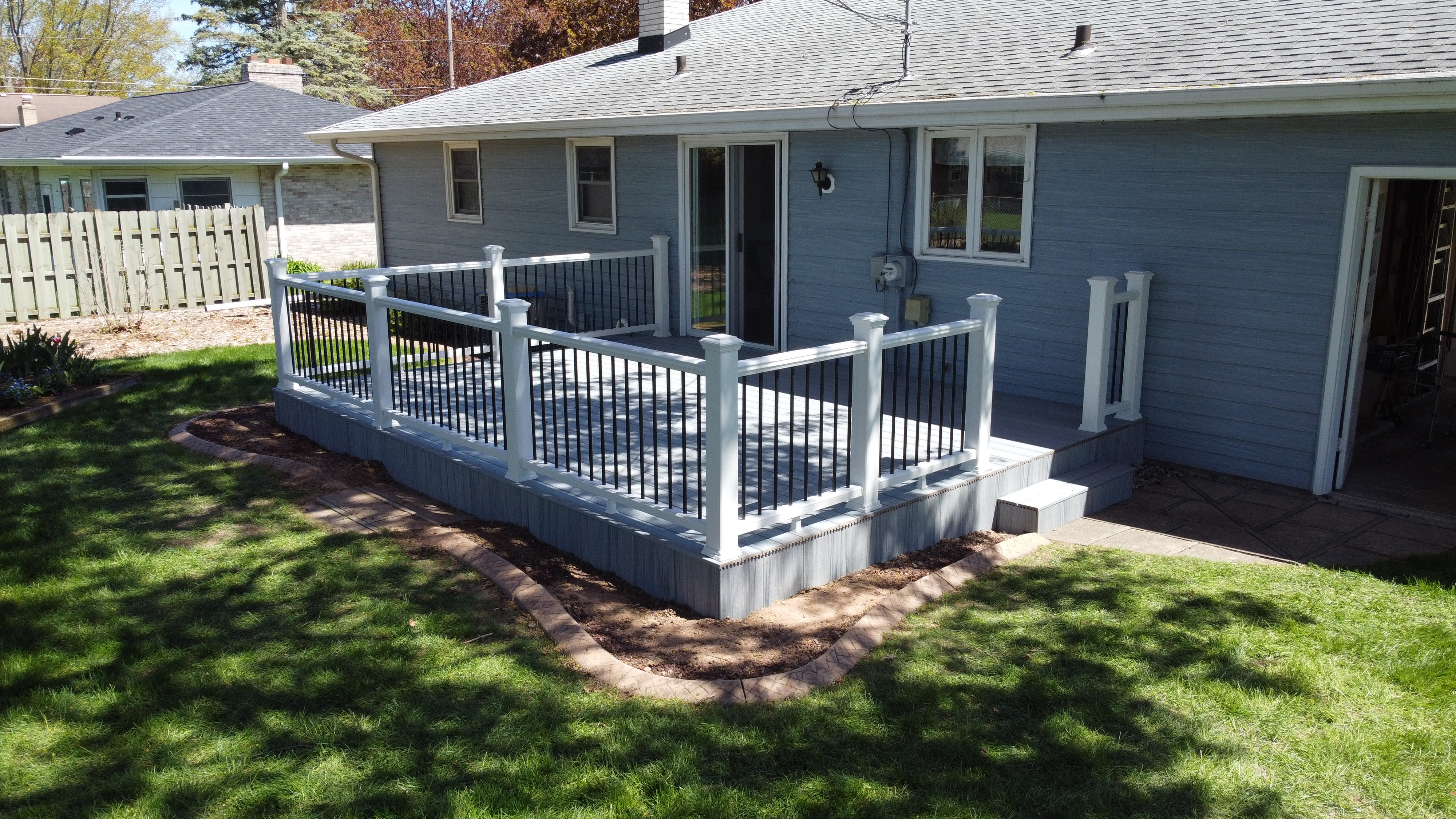 Ground Level Trex Enhance Naturals Foggy Wharf composite deck attached to a light blue house