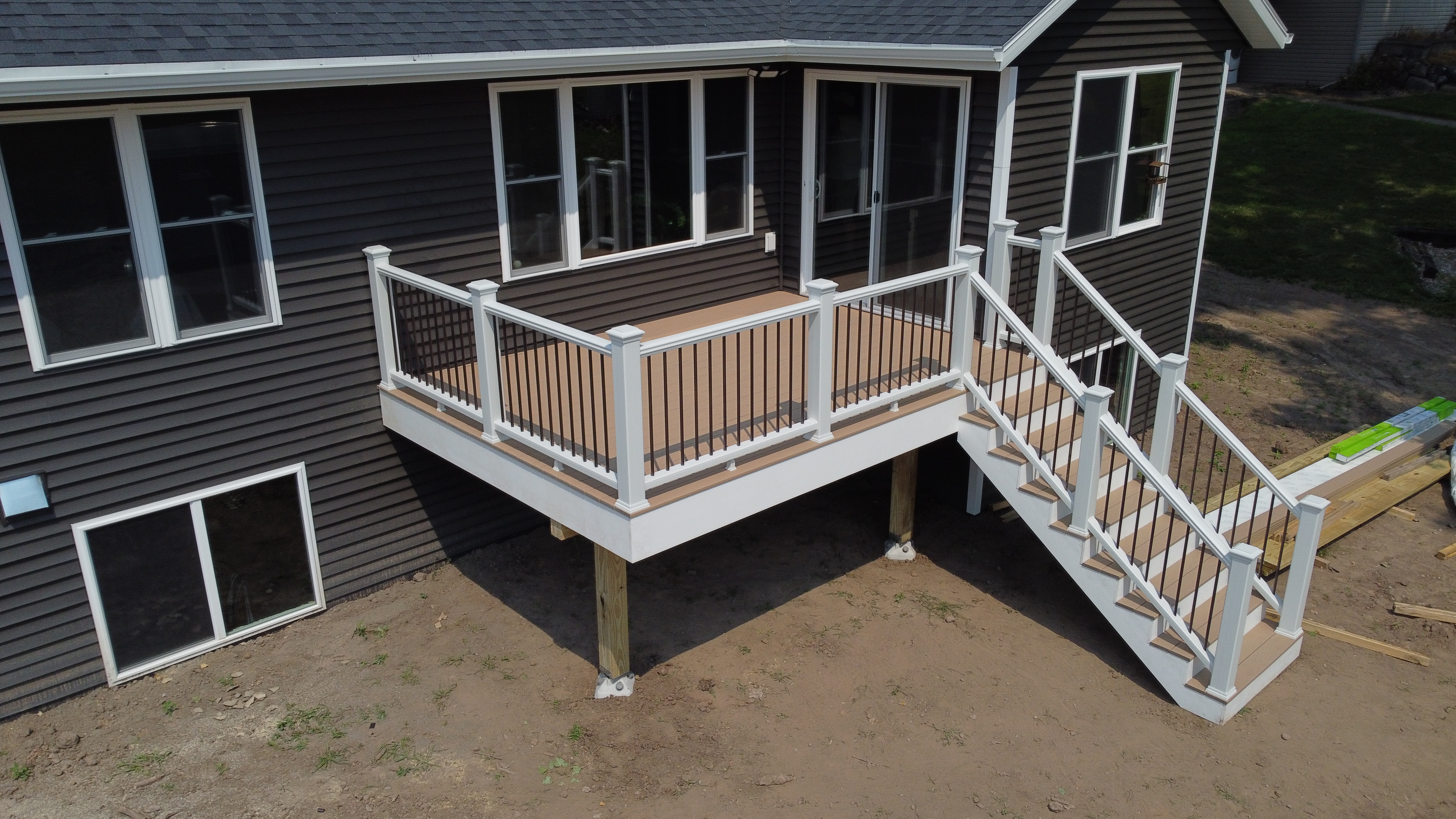 Deck builder Green Bay. Elevated Trex Transcend Lineage Carmel composite deck attached to a gray house built by the deck builder Nothin' but Decks in Howrad WI
